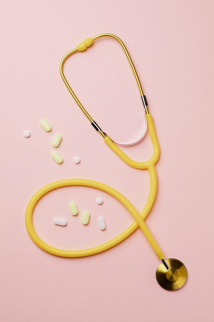 pexels-photo-4047077-4047077 Flat lay of a yellow stethoscope and assorted pills on a pastel pink background.